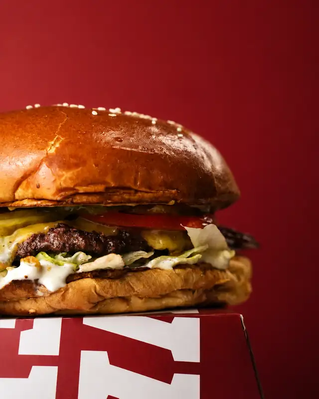 Burger wołowy z serem i sosem na tle czerwonej ściany